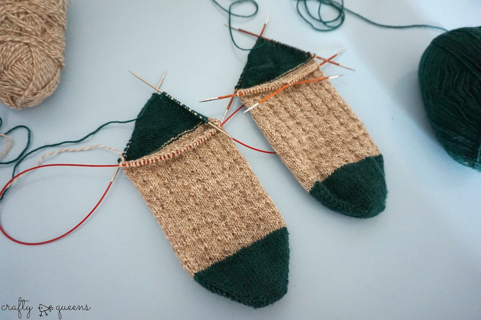 Two partially knit socks laying side by side, using different types of knitting needles