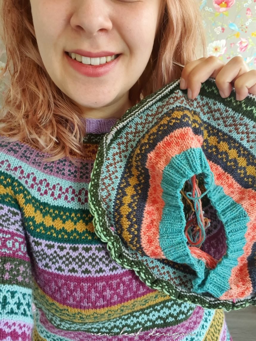 person wearing colourwork sweater while holding up new colourwork knitting project