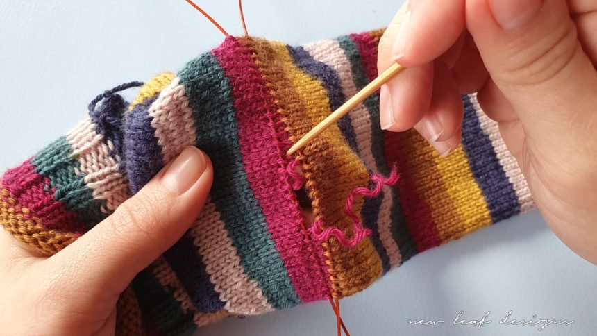 two hands holding sock tube, slowly unraveling yarn to create a gap for the heel