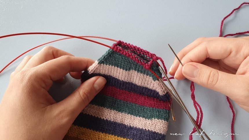 two hands holding up sock in progress, with tapestry needle ready for sewing